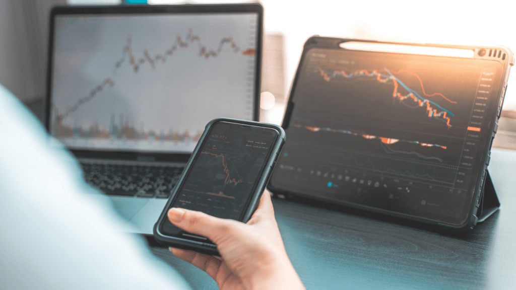 a person holding a smart phone in front of a stock market graph