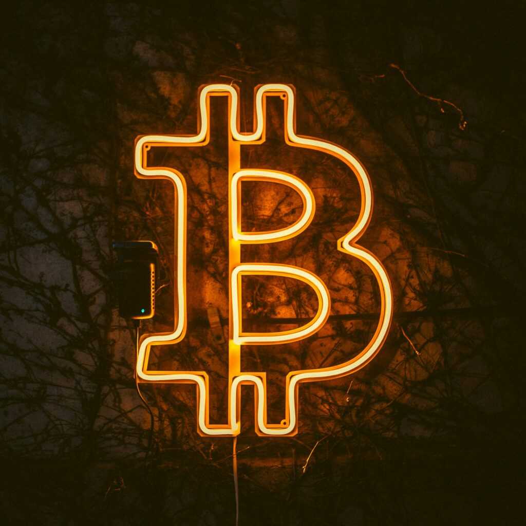 Illuminated orange neon Bitcoin sign on a dark wall, symbolizing digital currency market.