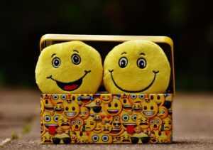 Two yellow smiley plush toys in an emoji-themed box, expressing fun and happiness.